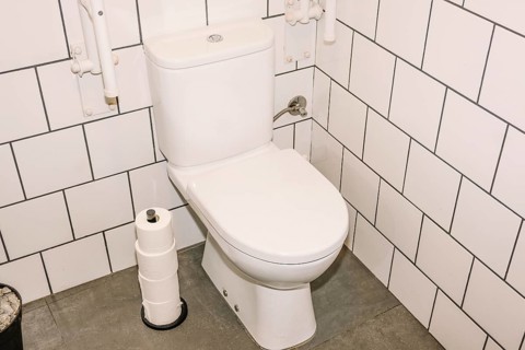 A clean white toilet in a coffee shop restroom, surrounded by white subway tiles and a gray floor.