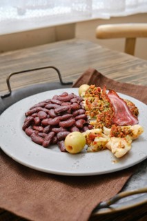 A plate with roasted fish and red beans, garnished with slices of bacon. The setting is warm and