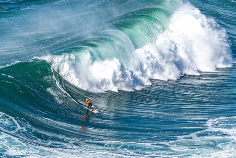 Surfers with their jet ski pilots in the Atlantic waves below Farol de Nazaré, Forte São Miguel,