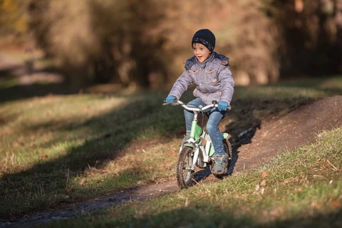 Six years old boy rides bicycle from the hill in the park