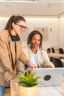 Two businesswomen collaborate on a laptop, utilizing a headset for communication in a modern office