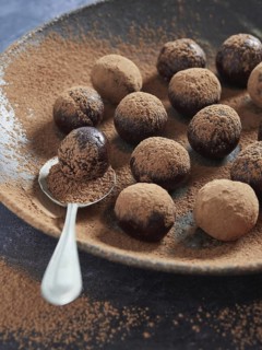 Chocolate bliss balls dusted with cacao on a dark plate with a spoon. Healthy homemade treat, sugar
