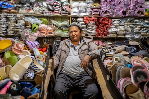 Man amidst many shoes and clothes, stall at the Osh Bazaar, Bishkek, Kyrgyzstan