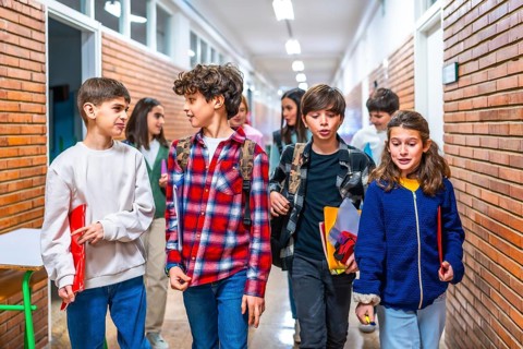Elementary school students carrying backpacks and notebooks walking down school hallway between