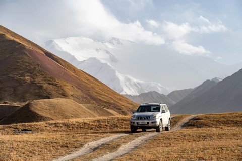 Off-road vehicle on a track between yellow meadows, glaciated high mountain peaks in the