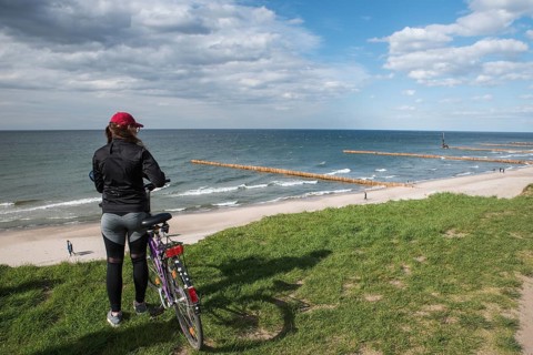 Woman with a bicycle stands on the top of a cliff and looks at the Baltic Sea and the beach