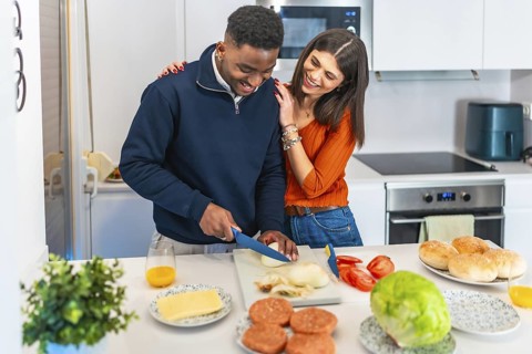 Young multiethnic couple preparing burgers, cutting onion and having fun in a modern kitchen