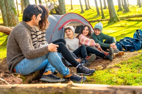 Parents talking with their three children sitting on camping tent enjoying a weekend trekking