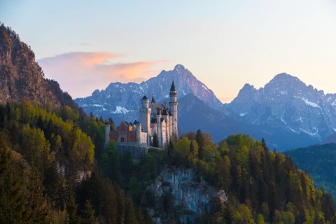 Neuschwanstein Castle surrounded by wooded mountains at dusk, Schwangau near Füssen, Ostallgäu