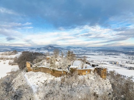 Aerial view of the snow-covered Hegau volcano Mägdeberg with remains of a castle wall on a cold