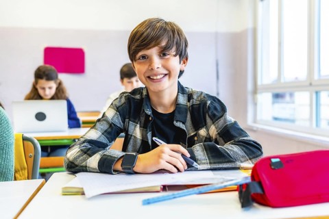 Happy student smiling while sitting at desk in classroom during lesson, with classmates in
