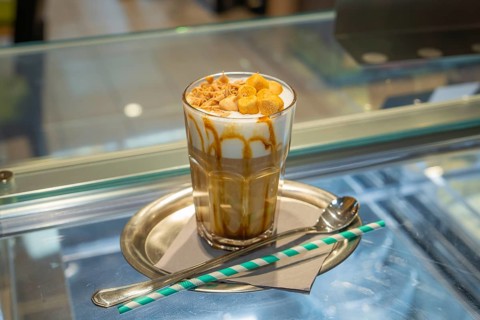 A glass of iced coffee with cream and caramel on a tray with straw and spoon, autumn creations,