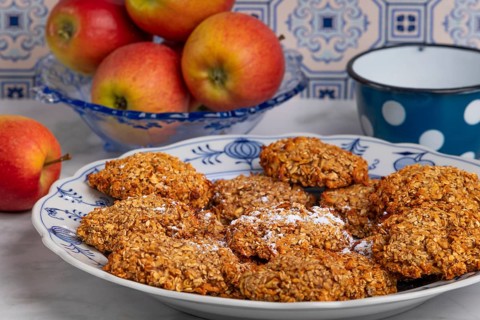 Freshly baked oat biscuits on a plate with apples in the background