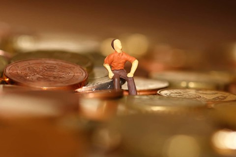Miniature man sitting among euro coins, North Rhine-Westphalia, Germany