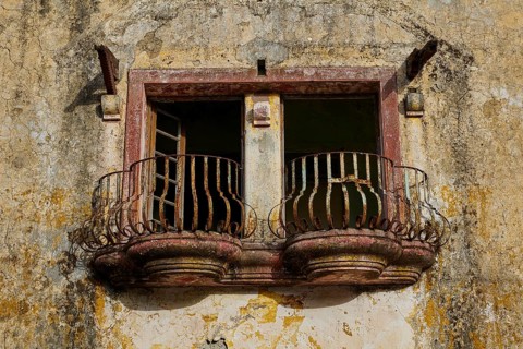 Detailed view of a ruined building with two small, decorated balconies and open windows, Italian