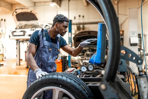 Young mechanic changing tire and using computer for diagnostics in a professional car workshop