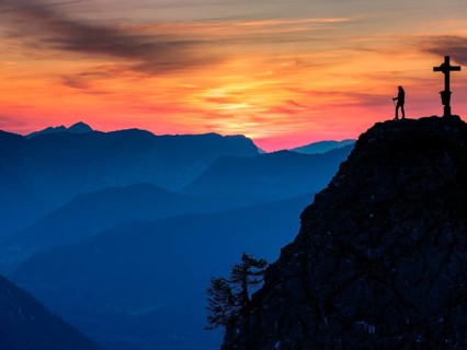 Mountaineer at the summit cross of the Kleiner Jenner at dusk, Reiteralpe in the background,