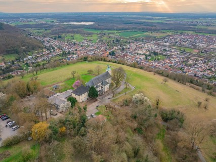 Wide bird's eye view of a hilly village backdrop with a striking building surrounded by nature,
