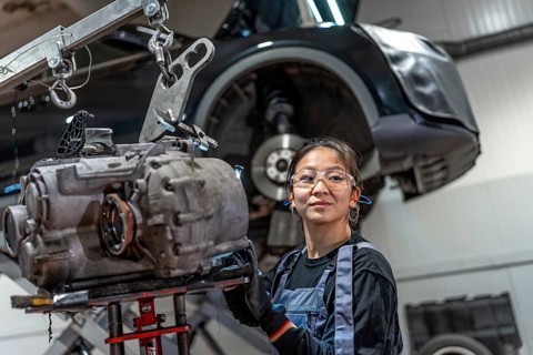 Young woman working on a gearbox with a crane in a professional car service, showcasing skills in