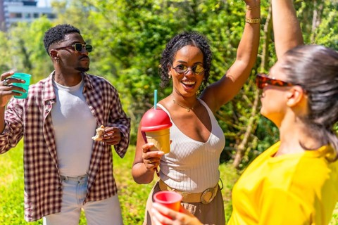 Young people enjoying fun moments, sipping drinks, and dancing joyfully in a park under the bright