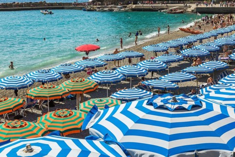Beach with bathers, tourists and blue parasols in late summer, Monterosso village, Cinque Terre, La