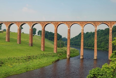 An old stone bridge with arches crossing a tranquil river in a green landscape, Aqueduct, Scottish