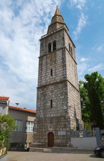 Historic stone bell tower with clear lines and slightly cloudy sky in the background, Church of St