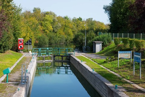 A quiet canal with a lock surrounded by lush vegetation and trees in autumn colours, Somme Canal,