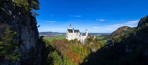 Panorama of Neuschwanstein Castle surrounded by forests and mountains under a blue sky, Schwangau,