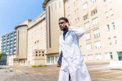 Busy african doctor talking to the mobile with serious expression walking outside the hospital