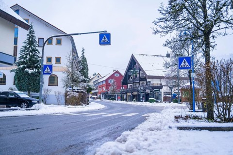 Snow-covered street in a village surrounded by traditional houses and road signs, Enzklösterle,