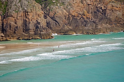 Küstenlandschaft mit türkisfarbenem Wasser und sandigem Strand, umgeben von imposanten Felsen,