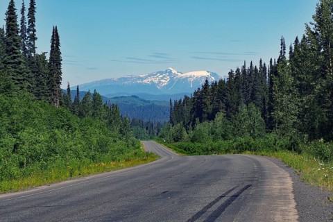 Narrow, traffic-free road leads through rugged mountain landscape, forest and snow-covered