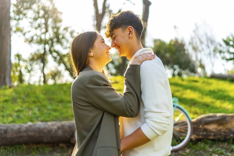 Smiling young couple enjoying a tender moment in a sunny park, surrounded by greenery and a bicycle