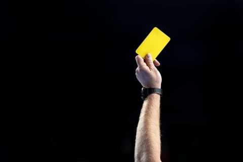 Referee's hand with yellow card with the black background