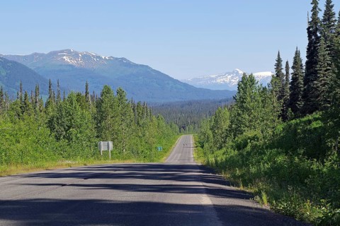 Road leads as an endless grade through forest and snow-capped mountains, wilderness, Stewart