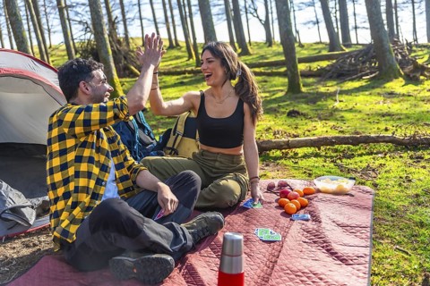 Happy couple sharing a joyful high five while camping, playing cards, and enjoying a picnic near