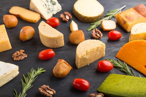 Set of different types of cheese with rosemary and tomatoes on a black wooden background. Side