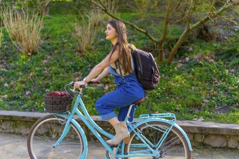 Young woman with backpack riding a vintage bicycle in a city park during a sunny spring day,