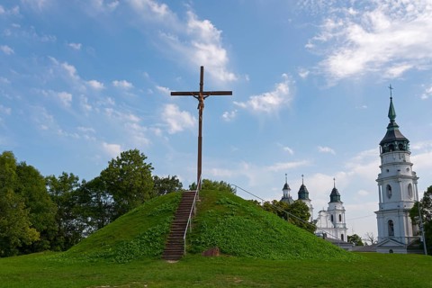 Cross on a green hill in front of a church with a blue sky in the background, Wysoka Górka, Wysoka
