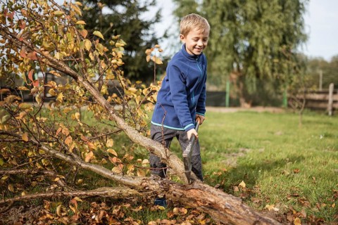 Seven year old smiling boy chopping a tree with an ax in the garden