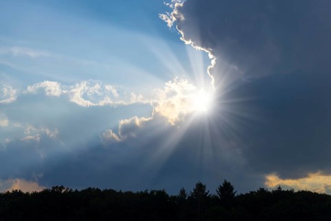 Rain clouds with sun shining through, sunbeams, blue sky, forest