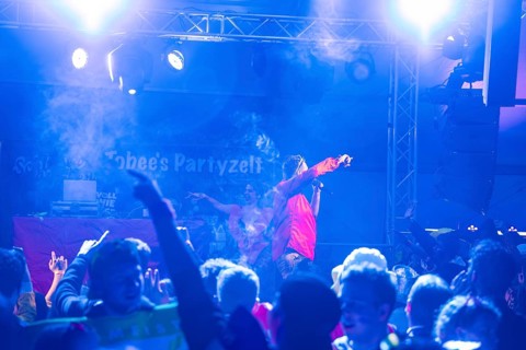 Schlager king Tobee performs in blue light in front of a rousing audience in a party tent,