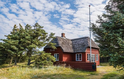 Red holiday home with thatched roof in a rural setting under a cloudy sky, Jutland, Denmark