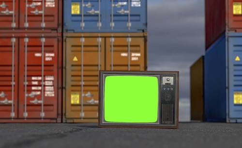 Vintage television with chroma green screen resting on shipping dock asphalt amongst stacked