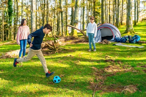 Caucasian young members of a family playing football in the forest together enjoying camping in the