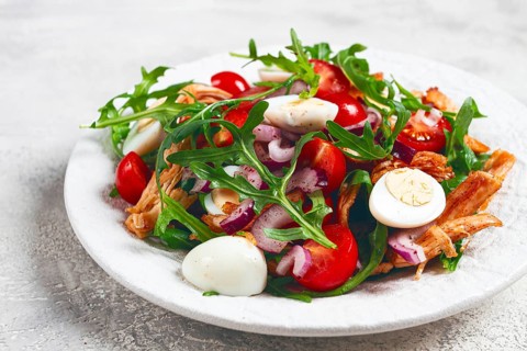 A warm salad with fried chicken fillet, arugula and cherry tomatoes, and boiled quail eggs, on a