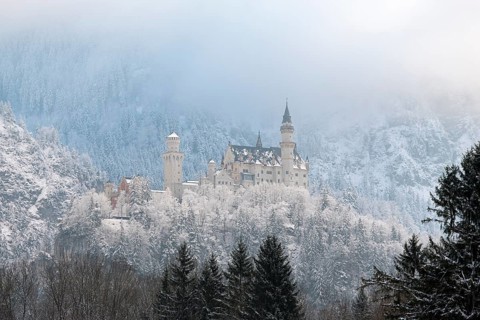 Mystical castle in wintry surroundings, framed by misty forests and mountain ranges,
