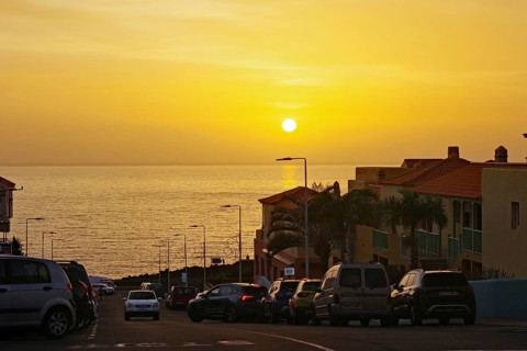 Road to a golden sunset over the sea with cars and buildings in the foreground, holiday resort Los