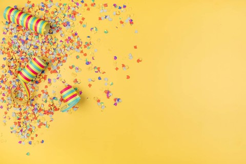 Colourful confetti and paper streamers scattered on a yellow background, carnival